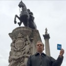 Peter Hitchens holding the letter H, standing with the statues of Nelson and King Charles I